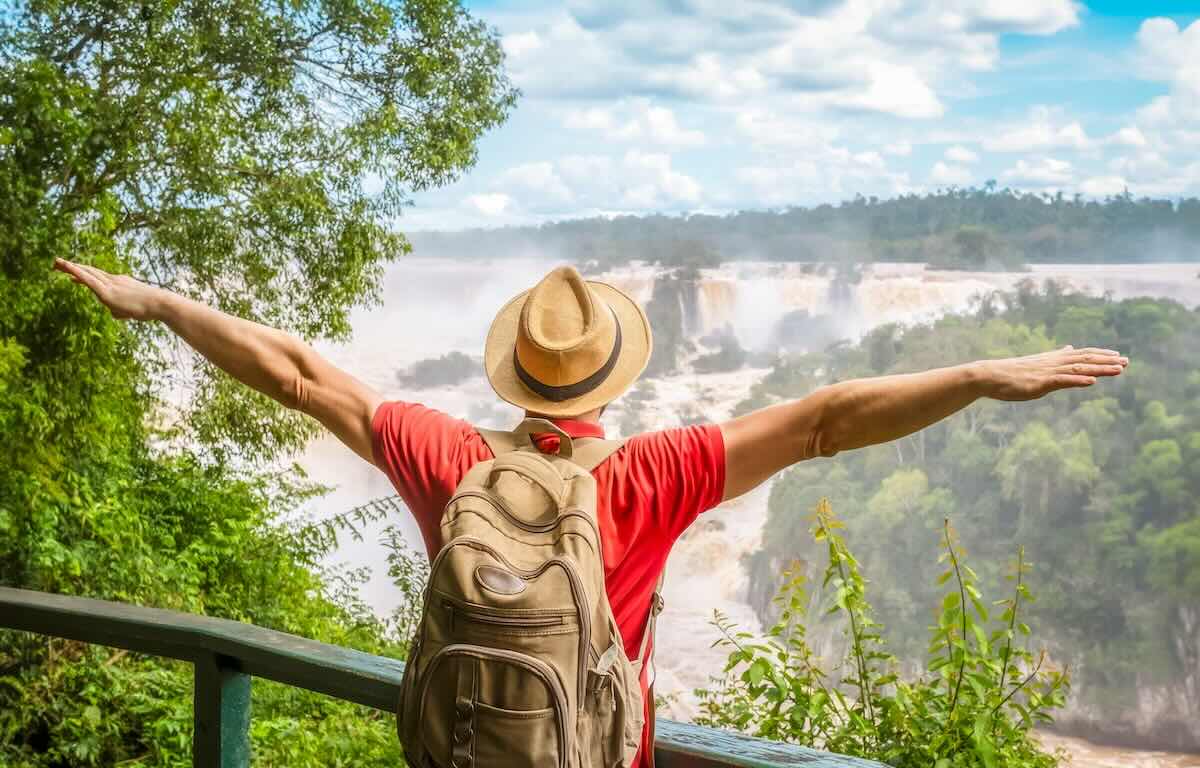 Iguazu Waterfalls, Brazil - Traveler man with raised arms watching Iguacu Falls in Brasil and Argentina